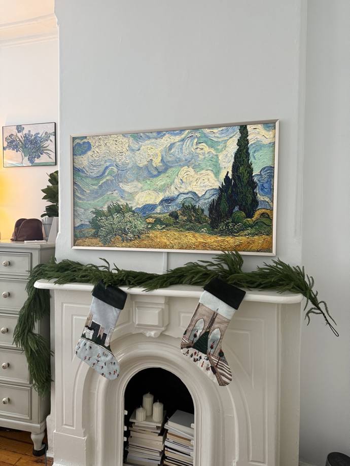Samsung Frame TV displaying Van Gogh art mounted above white fireplace mantle, NYC brownstone with Christmas decor