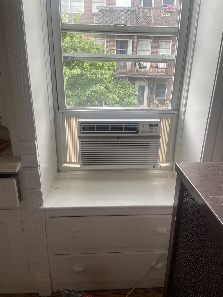 Window AC unit installed with support bracket in a NYC apartment