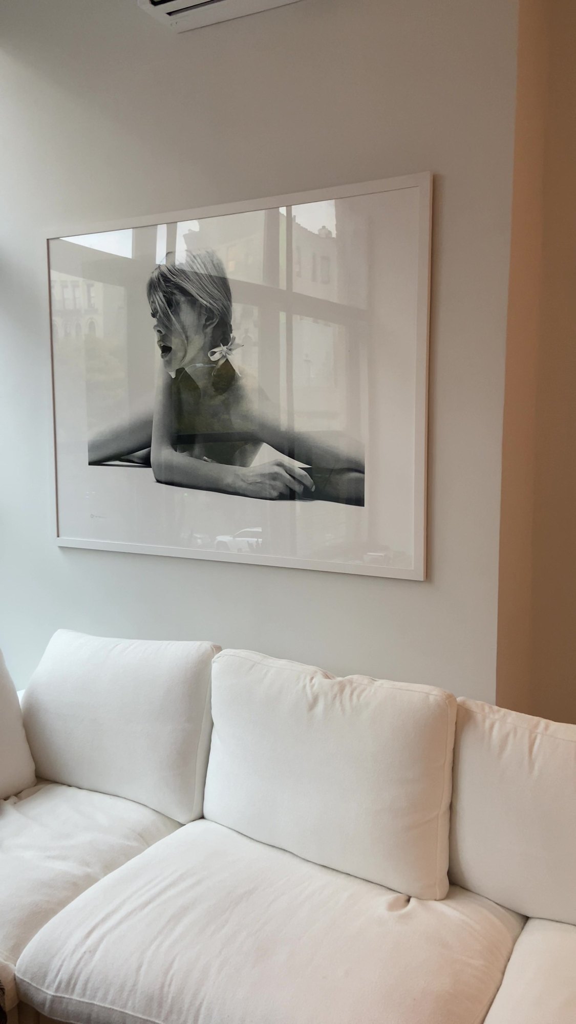 After: oversized black and white framed print mounted above a white sofa in a NYC apartment