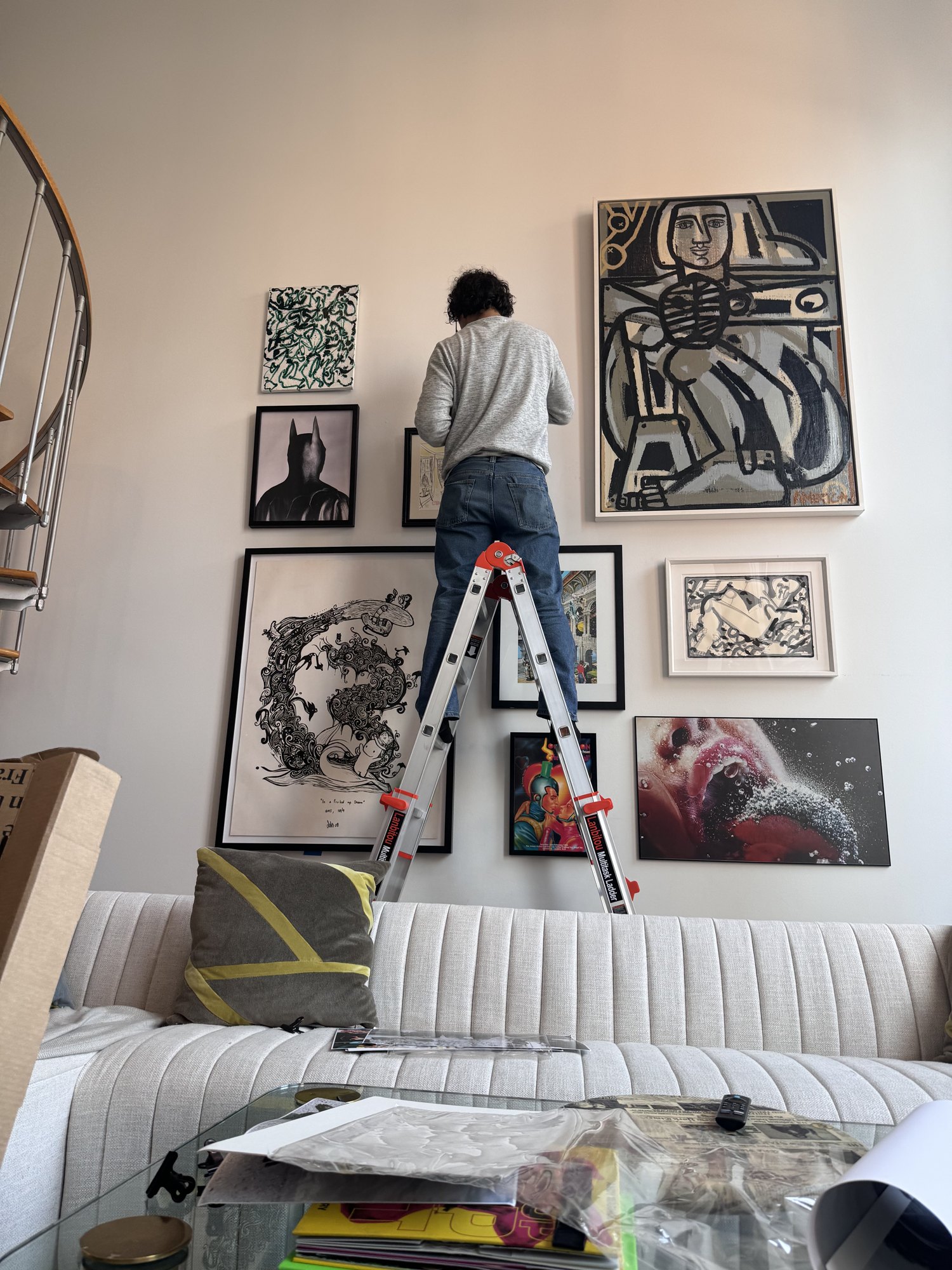 Gallery wall installation in progress on a ladder in a Manhattan living room