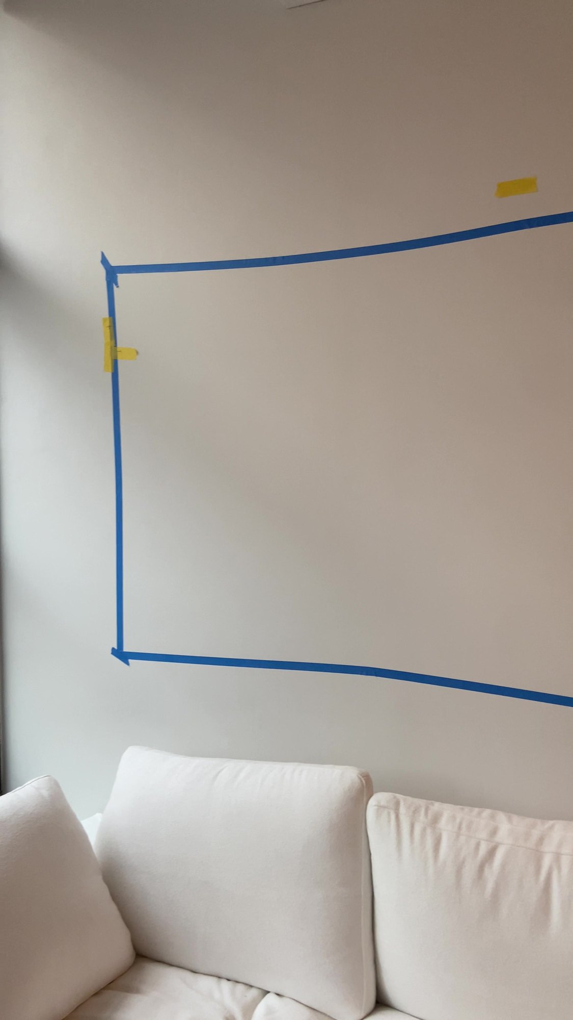 Before: blank living room wall with painter's tape marking where an oversized print will hang