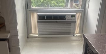 Window AC unit installed with support bracket in a NYC apartment